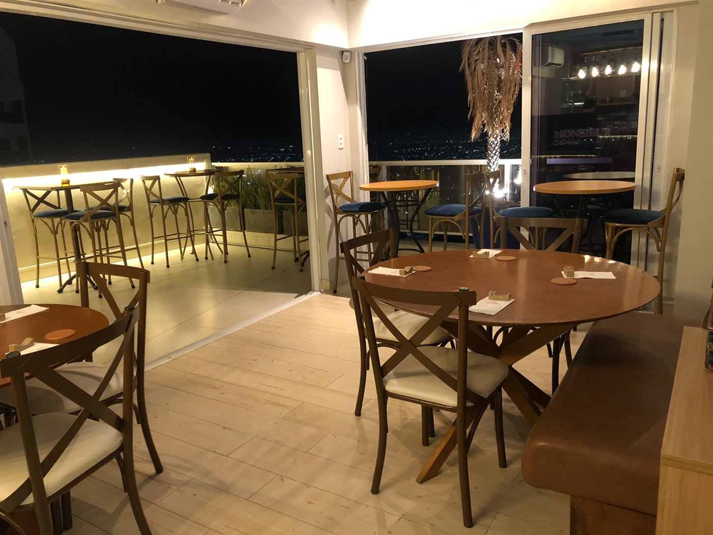 Salão com mesas postas e o terraço iluminado ao fundo