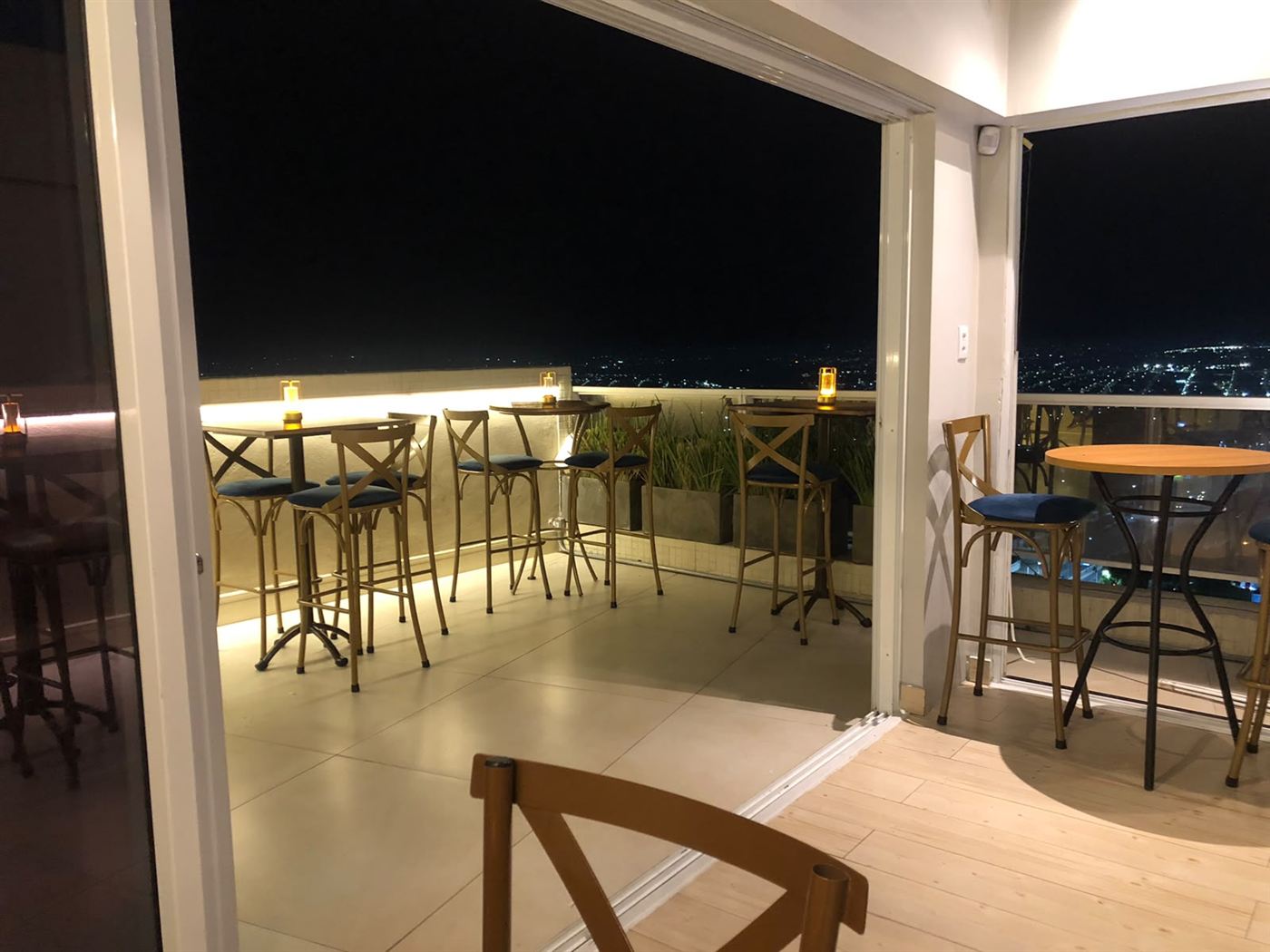 Terraço à noite com mesas altas e as luzes da cidade